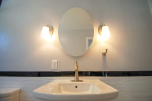 Oval mirror medicine cabinet with pedestal sink and sconce lights