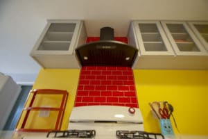 Candy apple red backsplash above oven with black hood and glass door cabinets
